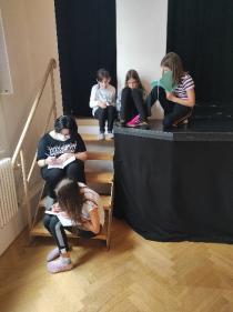 Mehrere Mädchen* sitzen auf einer Treppe, die zu einer Bühne führt und schreiben Tagebuch