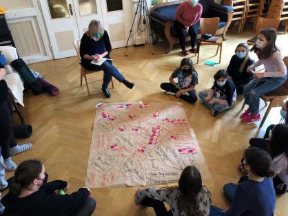 Die Gruppe sitzt um ein Plakat herum, auf dem Vor- und Nachteile von Mädchen*sein stehen.